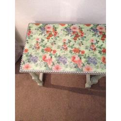 small table chalk painted light green with plastic flowered top edged with pewter nails